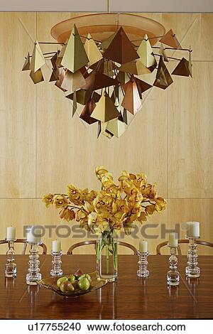 Stock Image - Metalworked light above centrepiece of cut flowers on table. Fotosearch