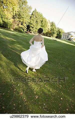 Stock Photo - Mid-adult bride running in park. Fotosearch