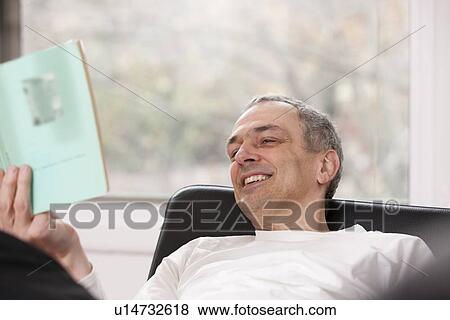 Stock Photo - Mid adult man relaxing at home reading a book. Fotosearch