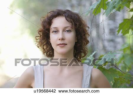Stock Image - Mid adult woman stands in nature looking directly at camera. Fotosearch