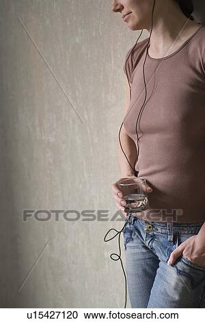 Stock Image - Mid section of redhead listening to headphones and holding glass of water. Fotosearch
