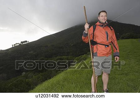 Stock Image - Middle-aged man stands on hillside in waterproof clothing. Fotosearch