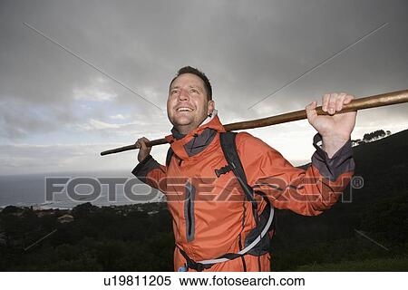 Stock Photography - Middle-aged man stands with walking staff in waterproof clothing. Fotosearch