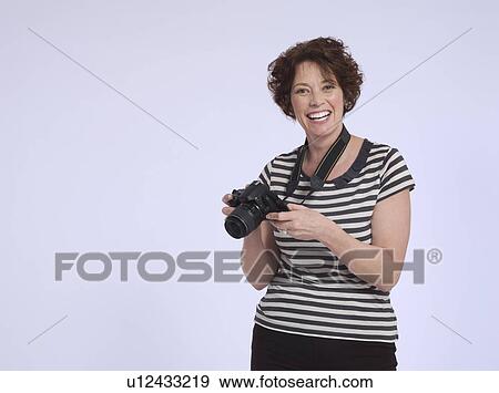 Stock Photo - Portrait of mid adult woman holding digital camera studio shot. Fotosearch