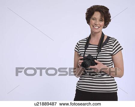 Stock Photo - Portrait of mid adult woman holding digital camera studio shot. Fotosearch