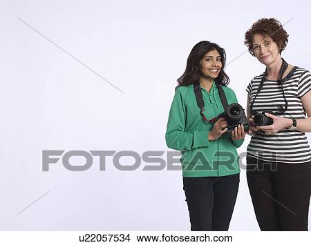 Picture - Portrait of two women holding digital cameras studio shot. Fotosearch