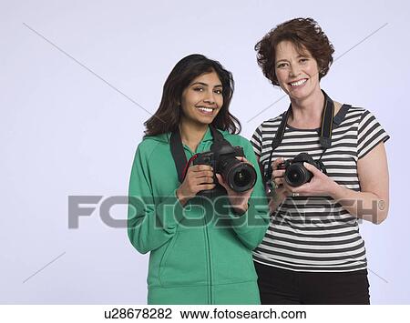 Stock Image - Portrait of two women holding digital cameras studio shot. Fotosearch