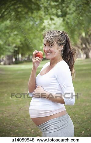 Pregnant woman in park eating apple View Large Photo Image Stock Photo - Pregnant woman in park eating apple. Fotosearch