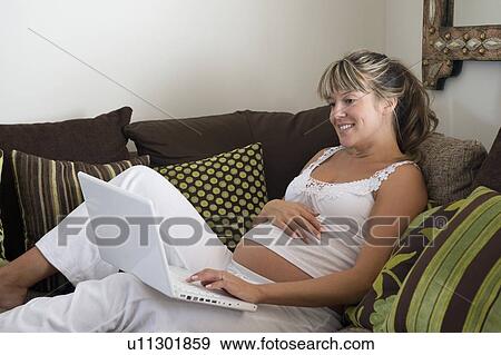 Pregnant woman reclining on sofa with laptop View Large Photo Image Stock Photo - Pregnant woman reclining on sofa with laptop. Fotosearch