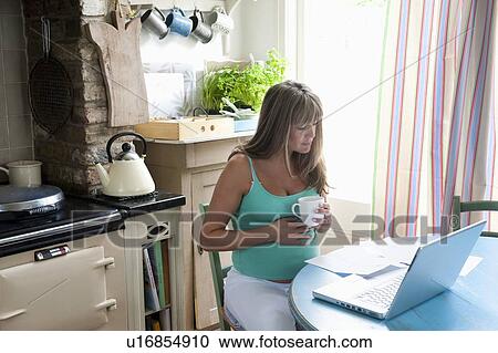 Pregnant woman sitting at kitchen table with laptop View Large Photo Image Stock Image - Pregnant woman sitting at kitchen table with laptop. Fotosearch