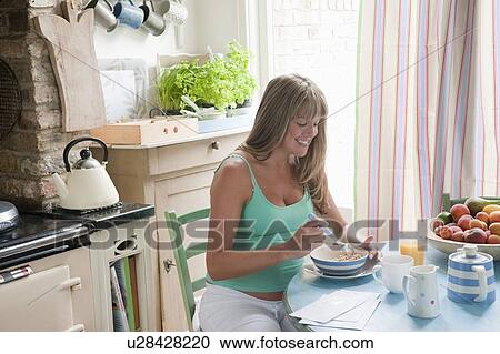 Stock Image - Pregnant woman sitting at kitchen table eating breakfast. Fotosearch