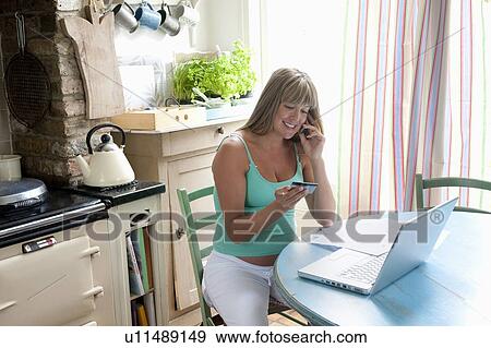 Stock Photo - Pregnant woman sitting at kitchen table with laptop. Fotosearch