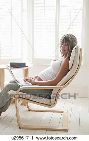 Stock Image - Pregnant woman sitting on chair using laptop. Fotosearch