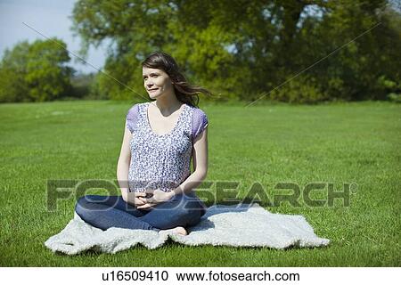 Stock Image - Pregnant woman sitting on grass. Fotosearch