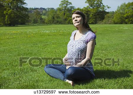 Stock Photo - Pregnant woman sitting on grass. Fotosearch