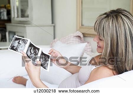 Stock Photo - Pregnant woman sitting on sofa with baby scan. Fotosearch