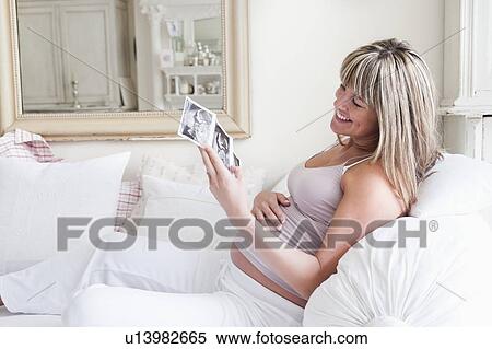 Pregnant woman sitting on sofa with baby scan photos View Large Photo Image Stock Photography - Pregnant woman sitting on sofa with baby scan photos. Fotosearch