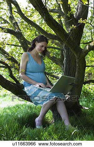 Stock Photograph - Pregnant woman using laptop in woods. Fotosearch