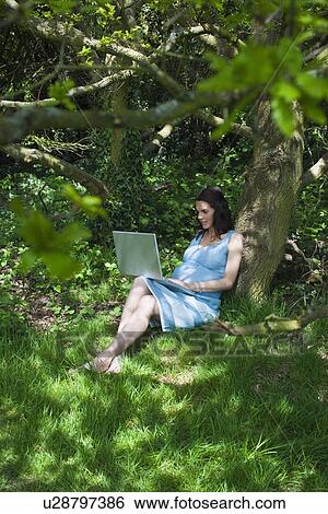 Stock Photograph - Pregnant woman using laptop in woods. Fotosearch