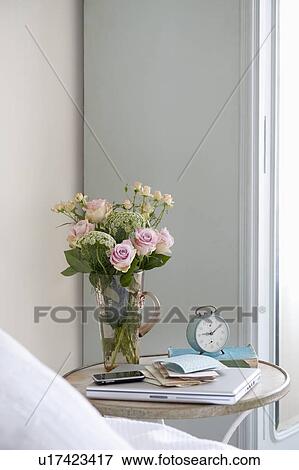 Stock Photo - Roses in vase on bedside table with books and alarm clock. Fotosearch