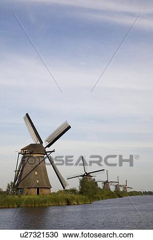 Stock Image - Row of windmills by river. Fotosearch