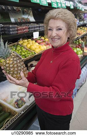 Senior woman holding pineapple in supermarket View Large Photo Image Stock Photography - Senior woman holding pineapple in supermarket. Fotosearch