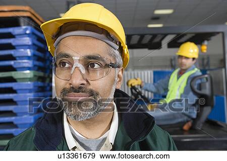 Serious man standing in factory wearing hart hat View Large Photo Image Stock Photo - Serious man standing in factory wearing hart hat. Fotosearch