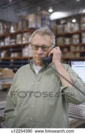 Stock Image - Serious man using telephone in distribution warehouse. Fotosearch