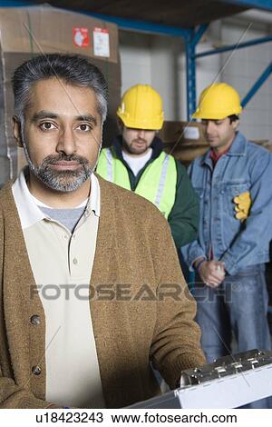 Serious men in factory colleagues in background View Large Photo Image Stock Image - Serious men in factory colleagues in background. Fotosearch