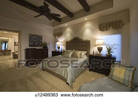 Stock Image - Silk bed cover on double bed in Palm Spring bedroom with beamed ceiling. Fotosearch