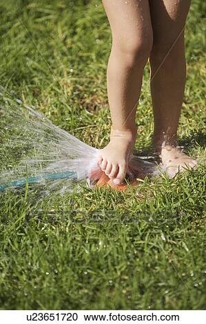 Stock Image - South Africa Cape Town girl playing with lawn sprinkler. Fotosearch