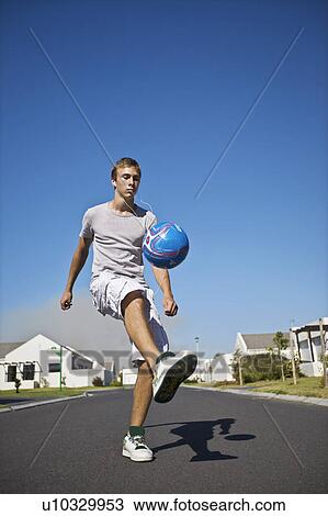 Stock Image - South Africa Cape Town teenage boy kicking ball on street. Fotosearch