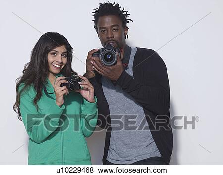 Stock Photo - Studio shot of young woman and mid adult man holding digital cameras. Fotosearch