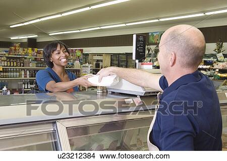 Picture - Supermarket employee hands product to customer in supermarket delicatessen. Fotosearch