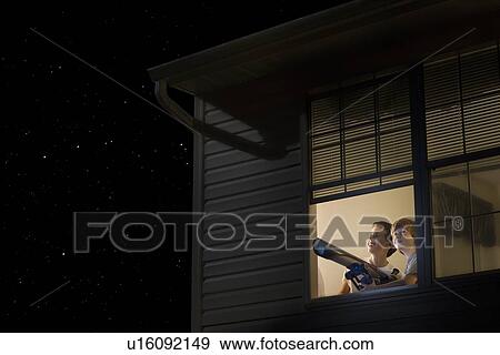 Stock Photo - Teenage boys stand with telescope at open window looking at night sky. Fotosearch