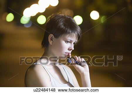 Stock Photo - Teenage girl stands thinking with mobile phone in street. Fotosearch