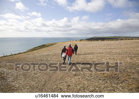 Picture - Three adults walk along a coastal cliff. Fotosearch