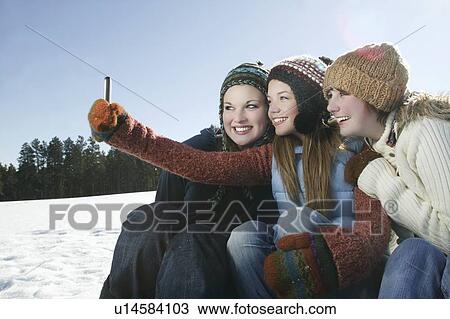 Stock Image - Three girls take self portrait with camera phone. Fotosearch