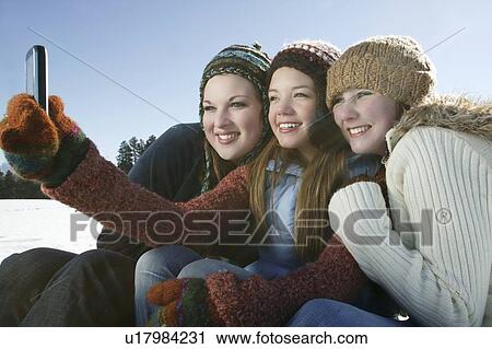 Stock Image - Three girls take self portrait with camera phone. Fotosearch