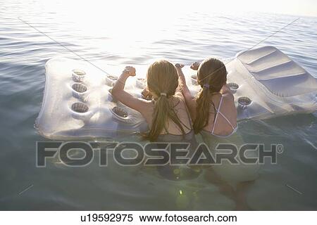 Twin sisters on air bed in evening light View Large Photo Image Stock Photography - Twin sisters on air bed in evening light. Fotosearch