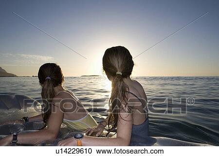 Stock Image - Twin sisters on air bed look back at land. Fotosearch