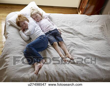 Stock Photo - Two sisters lie sleeping on a bed elevated view. Fotosearch