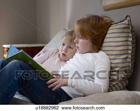 Two sisters sit reading on a single bed View Large Photo Image Stock Image - Two sisters sit reading on a single bed. Fotosearch