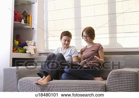 Stock Image - Two teenage girls looking at photo album on sofa. Fotosearch
