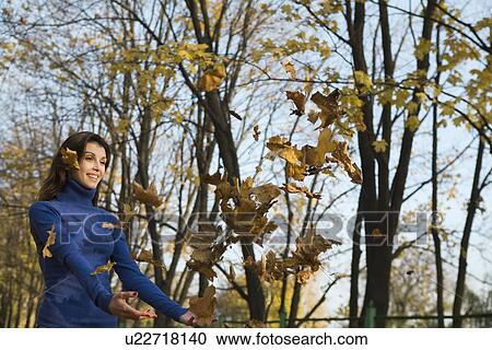 Woman catching falling leaves in park View Large Photo Image Stock Image - Woman catching falling leaves in park. Fotosearch