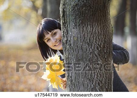 Stock Photo - Woman holding leaves behind tree in park. Fotosearch
