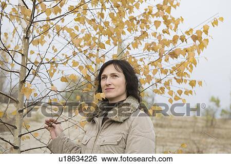 Stock Photograph - Woman holding tree in field. Fotosearch