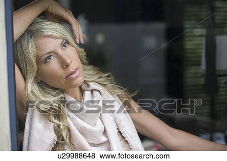 Stock Photo - Woman leans on arm at window eith a faraway look in her eyes. Fotosearch