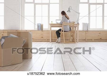 Woman sits at desk in window area of loft apartment View Large Photo Image Stock Image - Woman sits at desk in window area of loft apartment. Fotosearch