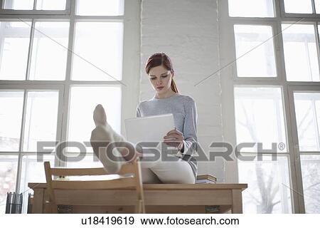 Woman sits on desk with laptop in loft apartment View Large Photo Image Stock Photo - Woman sits on desk with laptop in loft apartment. Fotosearch